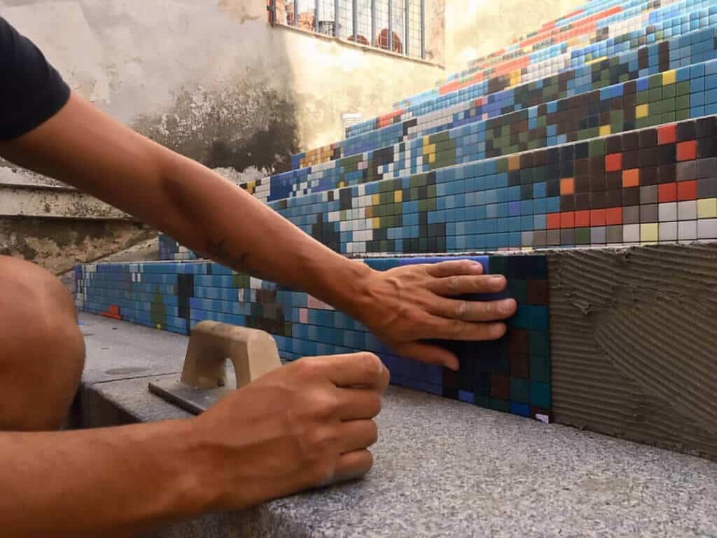 A mosaic tile installer installing blue mosaic tiles on a wall with a trowel and adhesive