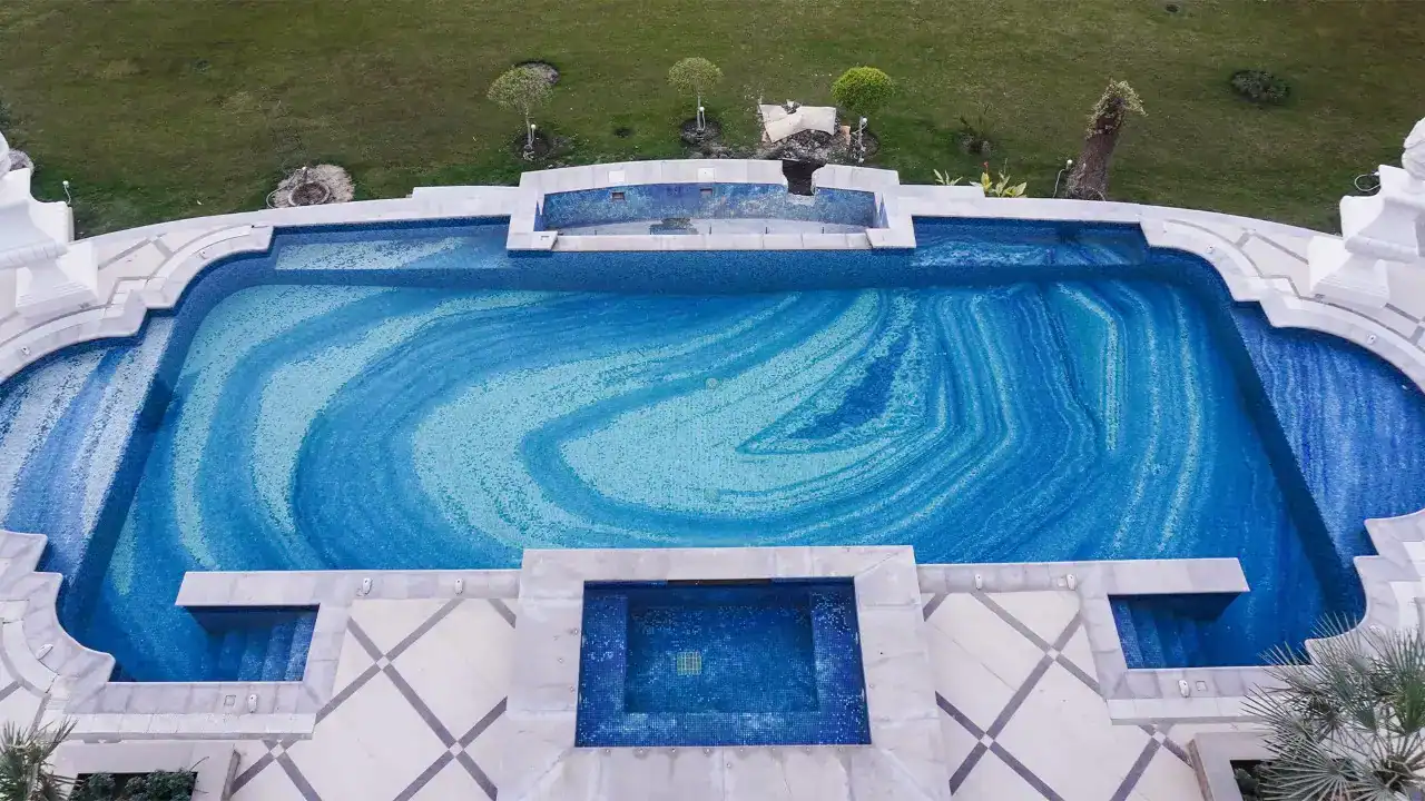 Luxurious outdoor pool with intricate blue mosaic tile pattern and surrounding marble deck design.