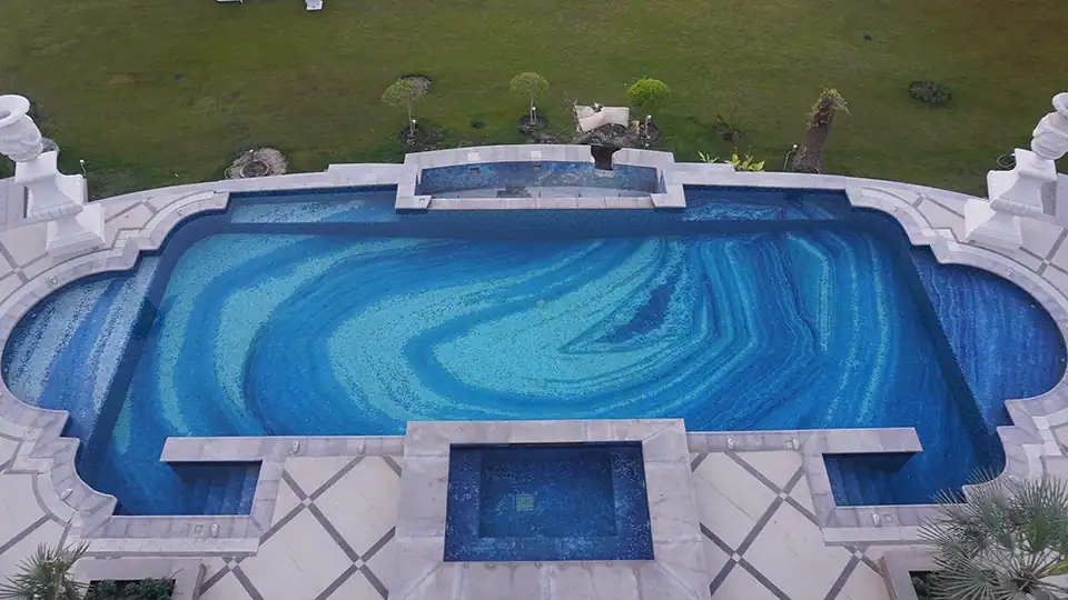 Luxury pool with abstract gradient mosaic tile art in swirling blue tones and marble border.