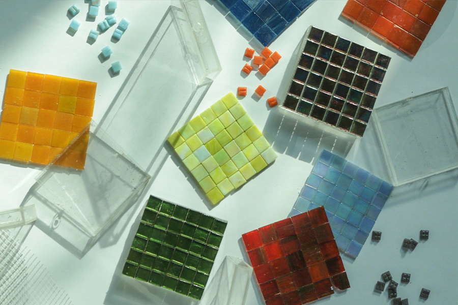 Assorted glass mosaic tile samples in vibrant colors, arranged with clear boxes on a white background.