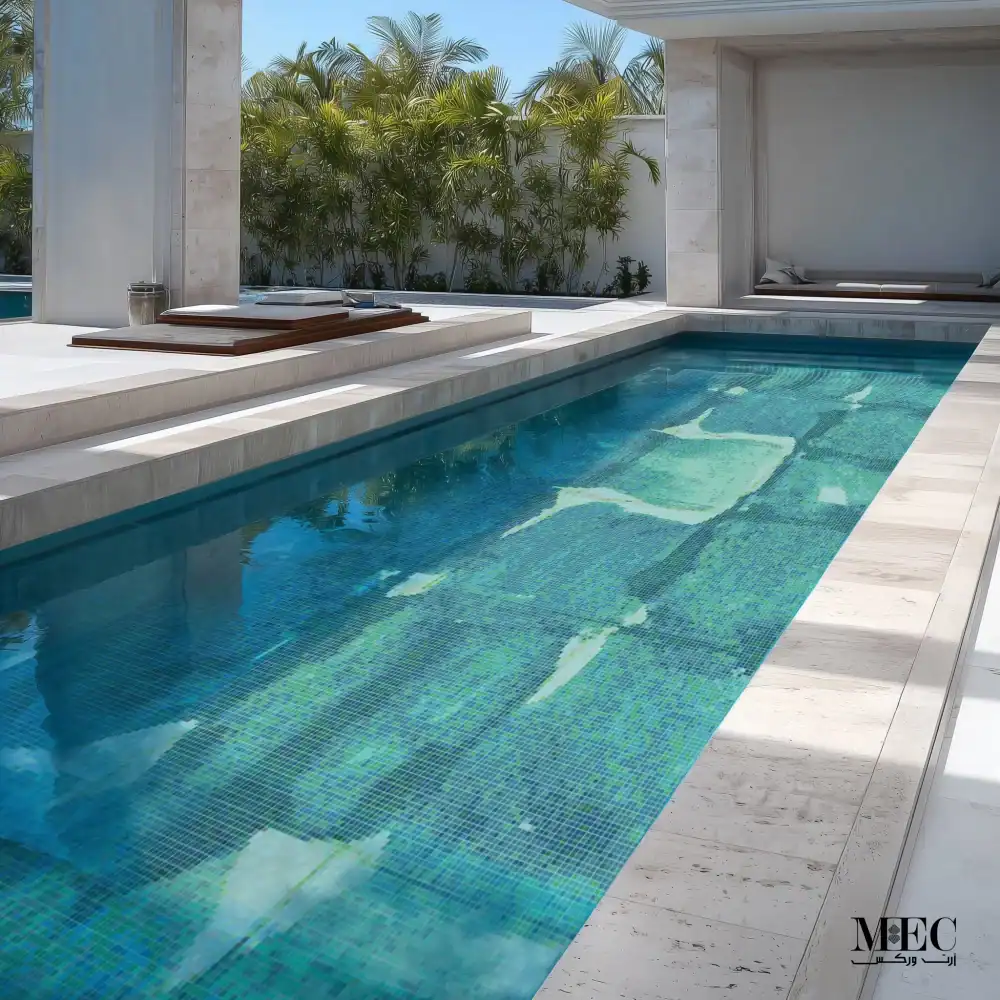 Luxury swimming pool with green and aqua mosaic tile design, sleek modern layout, and resort-style lounging area surrounded by tropical plants.