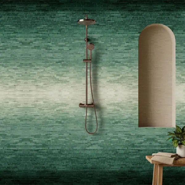 Emerald Tide Mosaic Shower space with a green gradient mosaic wall transitioning from dark forest tones to light beige, featuring a bronze shower fixture, arched niche, and wooden bench with towels.