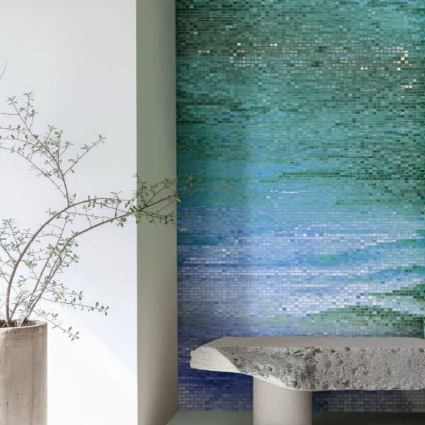 Ocean Mist Mosaic Wall Modern interior featuring a glass mosaic wall with a blue-to-turquoise gradient resembling calm water, paired with a sculptural stone bench and minimalist decor.