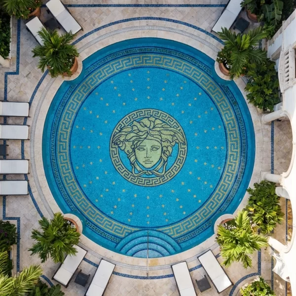 Round turquoise pool mosaic with central Medusa face motif, Greek key border ring, and small gold star accents in luxury courtyard pool design.