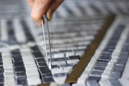 Crafting Your Masterpiece- MEC Artworks Close-up of artisan placing mosaic tile with tweezers, showcasing intricate craftsmanship and design precision.