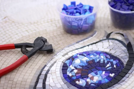 Tailored Design & Proposal- MEC Artworks Mosaic in progress with blue tiles, red pliers, and tools used for precise tile cutting.